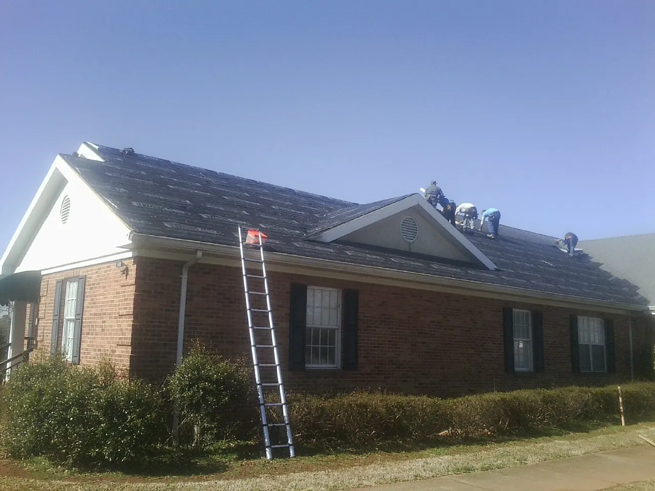 Crew tearing shingles off a brick ranch roof with a ladder set — Emergency Roof Repair work by our crew in Fairbury