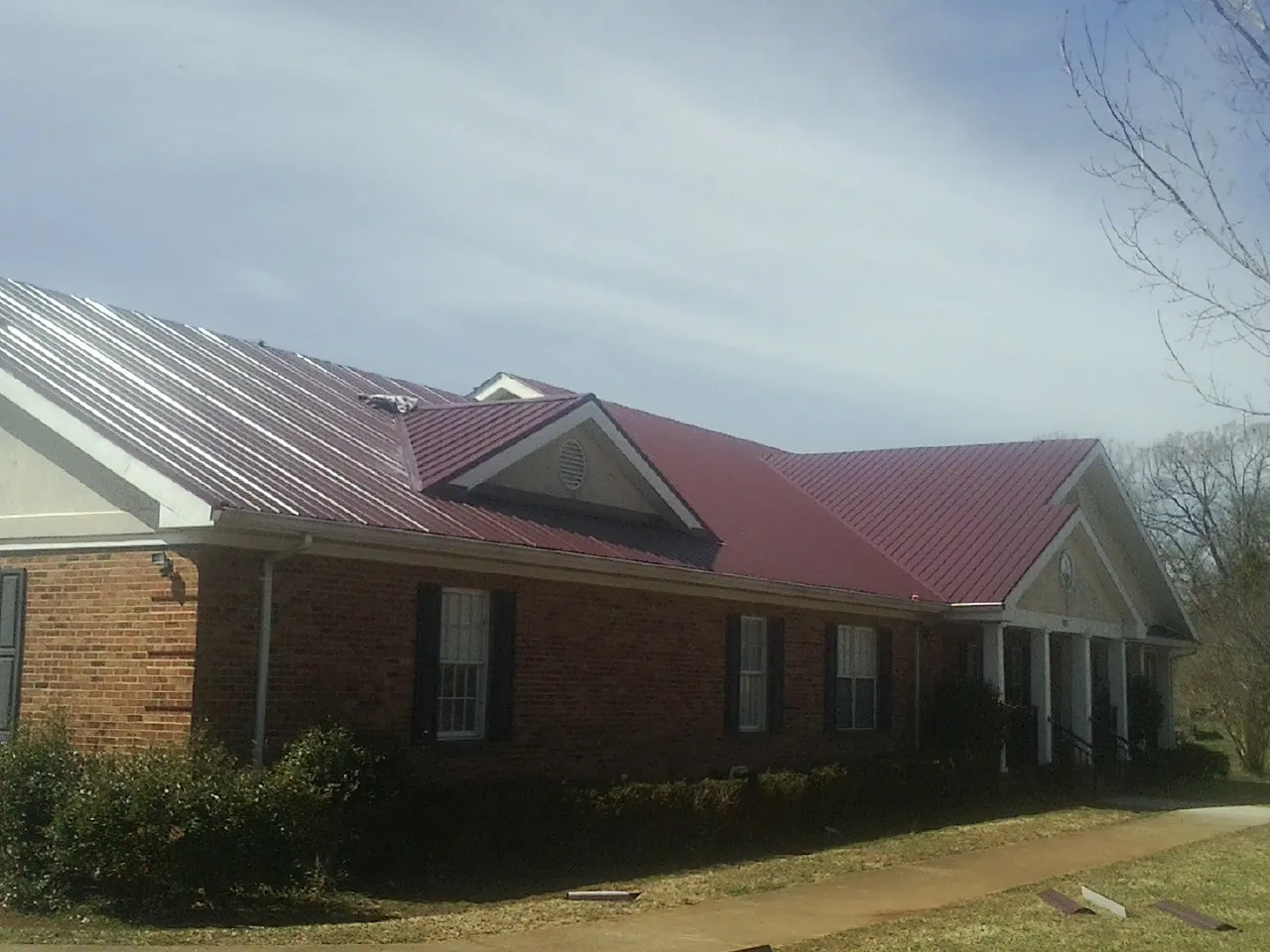 Red metal roof with gabled entries on a long brick building, from a Hail Damage Roof Repair job in Fairbury