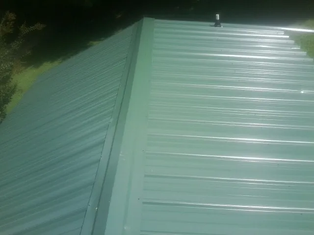 New green metal panels meeting at the ridge of a roof — Flat Roof Repair work by our crew in Fairbury