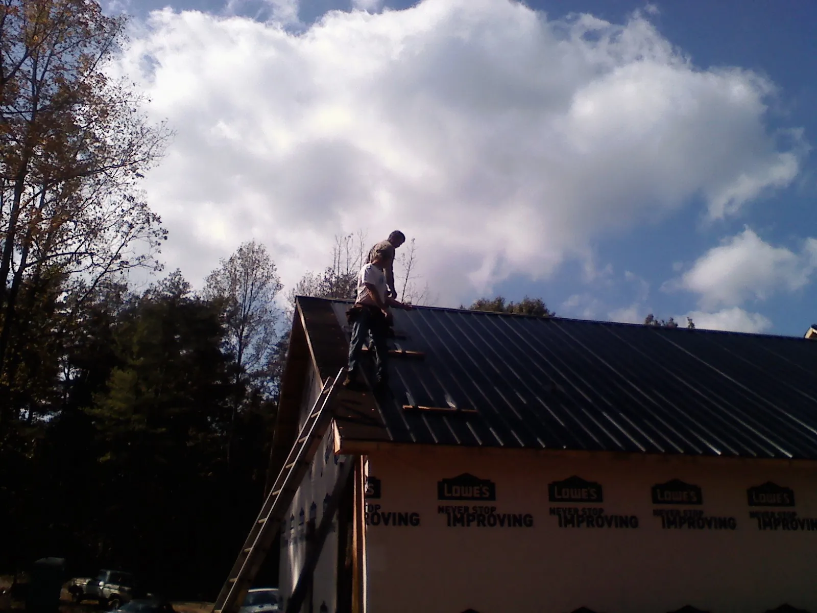 Roofer fastening dark metal panels high against a cloudy sky, from a Roof Inspection job in Fairbury