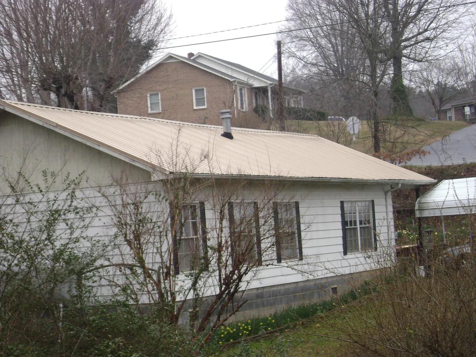 Tan metal roof on a white sided house set into a hillside — Commercial Roofing by Roofing Brothers in Fairbury