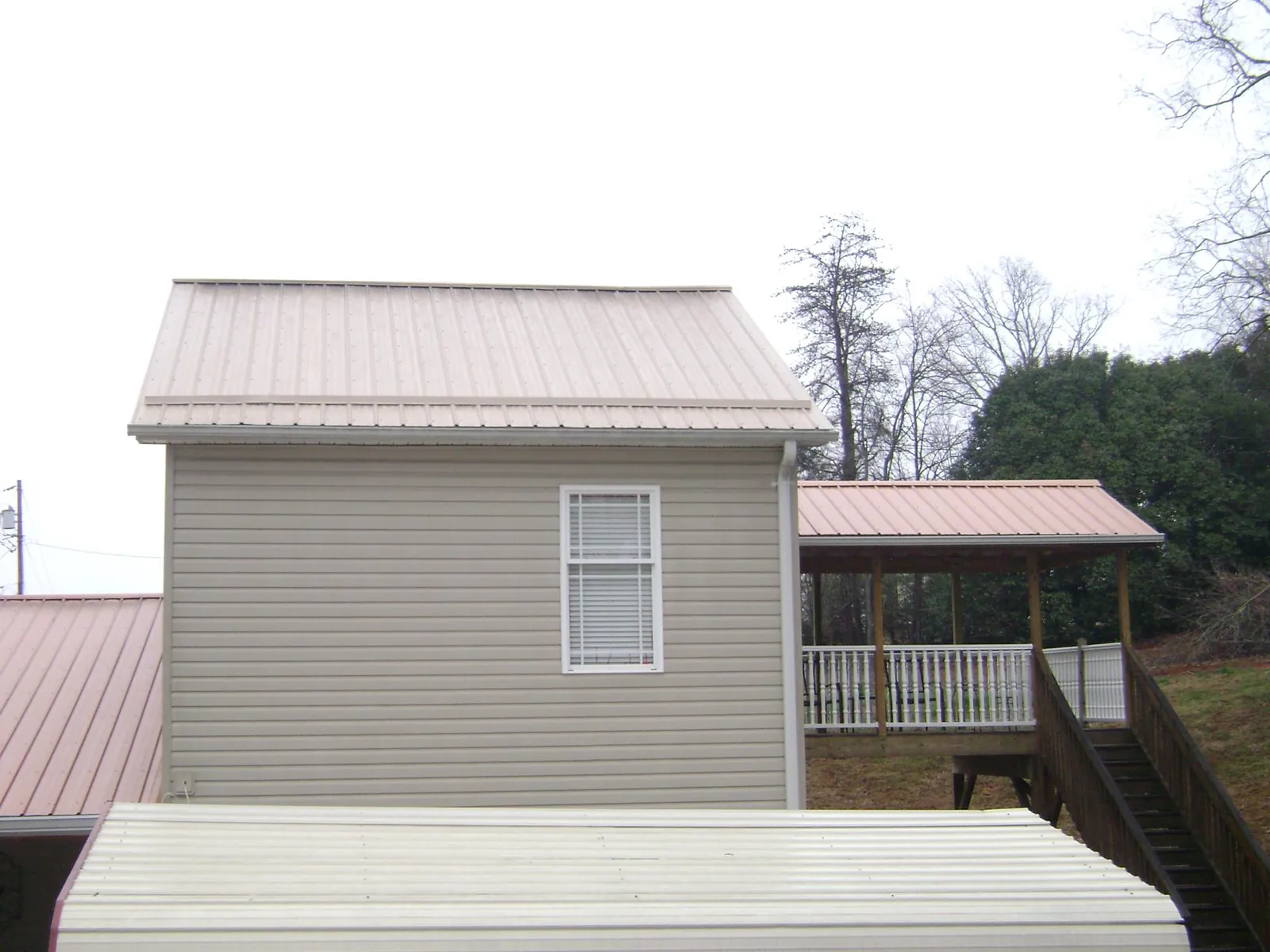 Tan metal roofs on a two story addition and attached porch, from a Roof Replacement job in Fairbury